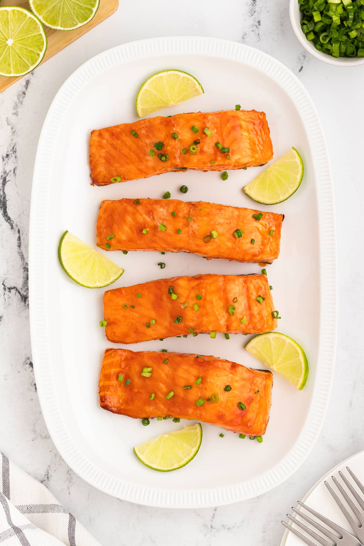 Four Honey Glazed Salmon fillets on a white plate with lime wedges