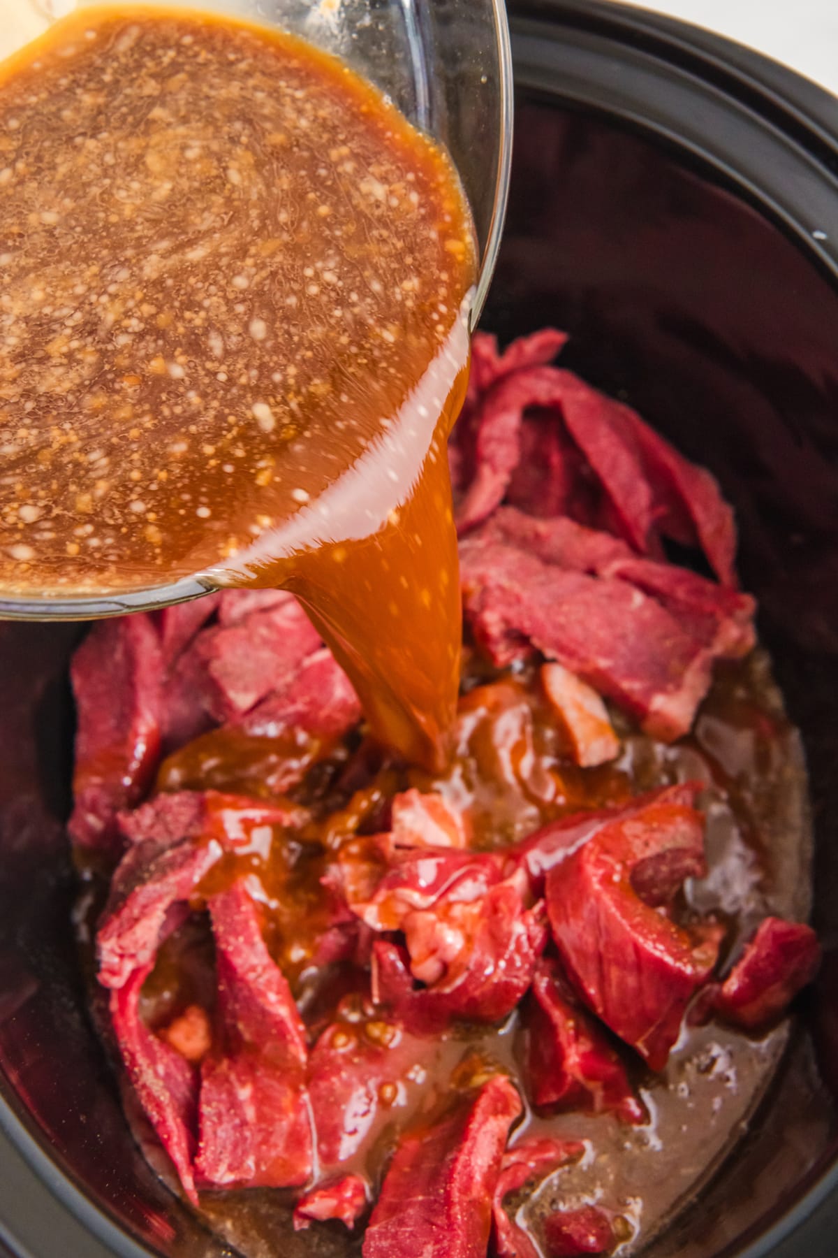 A sauce being poured over beef in a slow cooker is another process in preparing Slow Cooker Beef and Broccoli