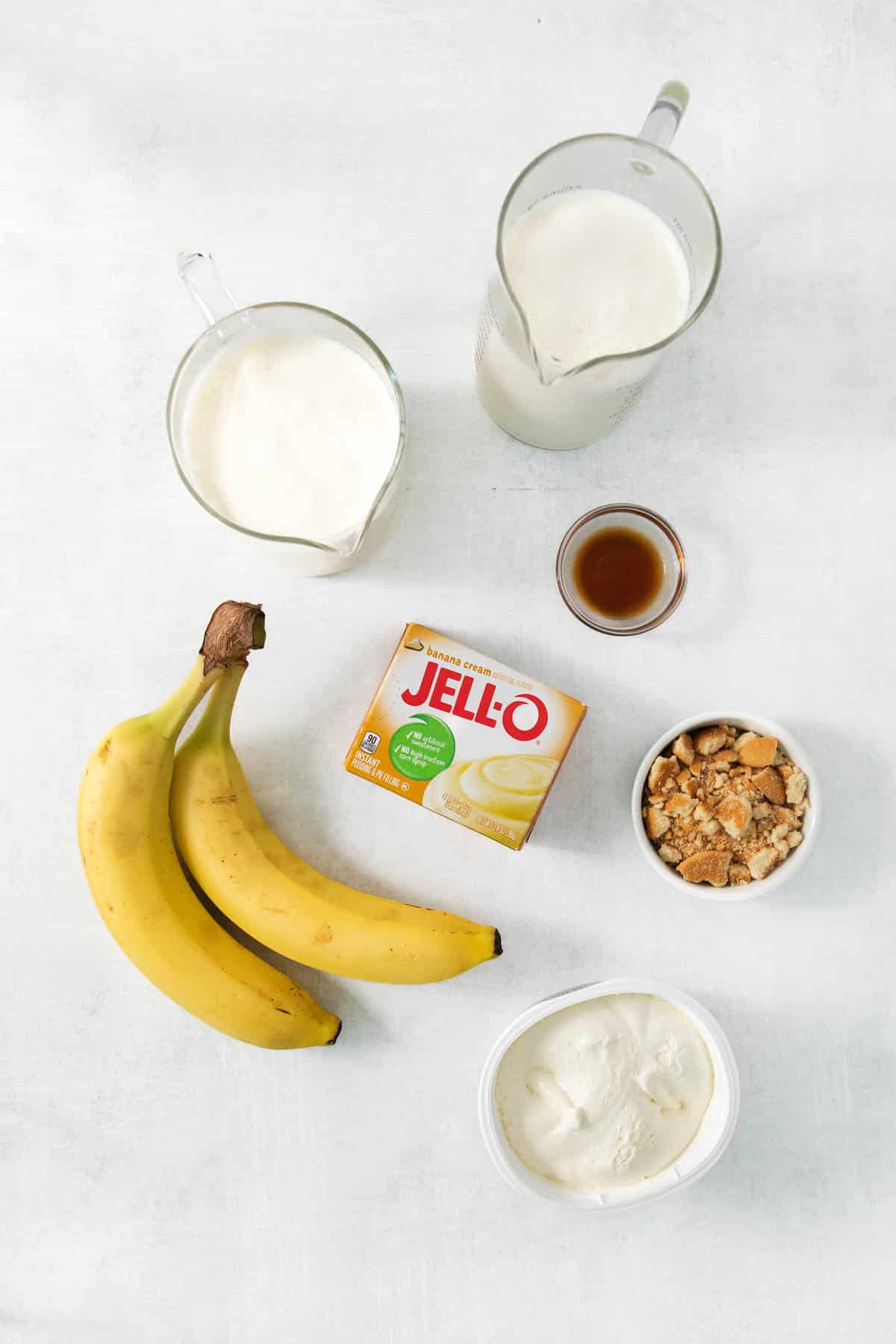 Bananas, yogurt, granola and other ingredients are laid out on a white surface.