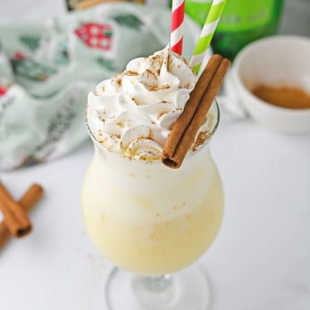 Eggnog float in curved glass with whipped cream and cinnamon sticks.