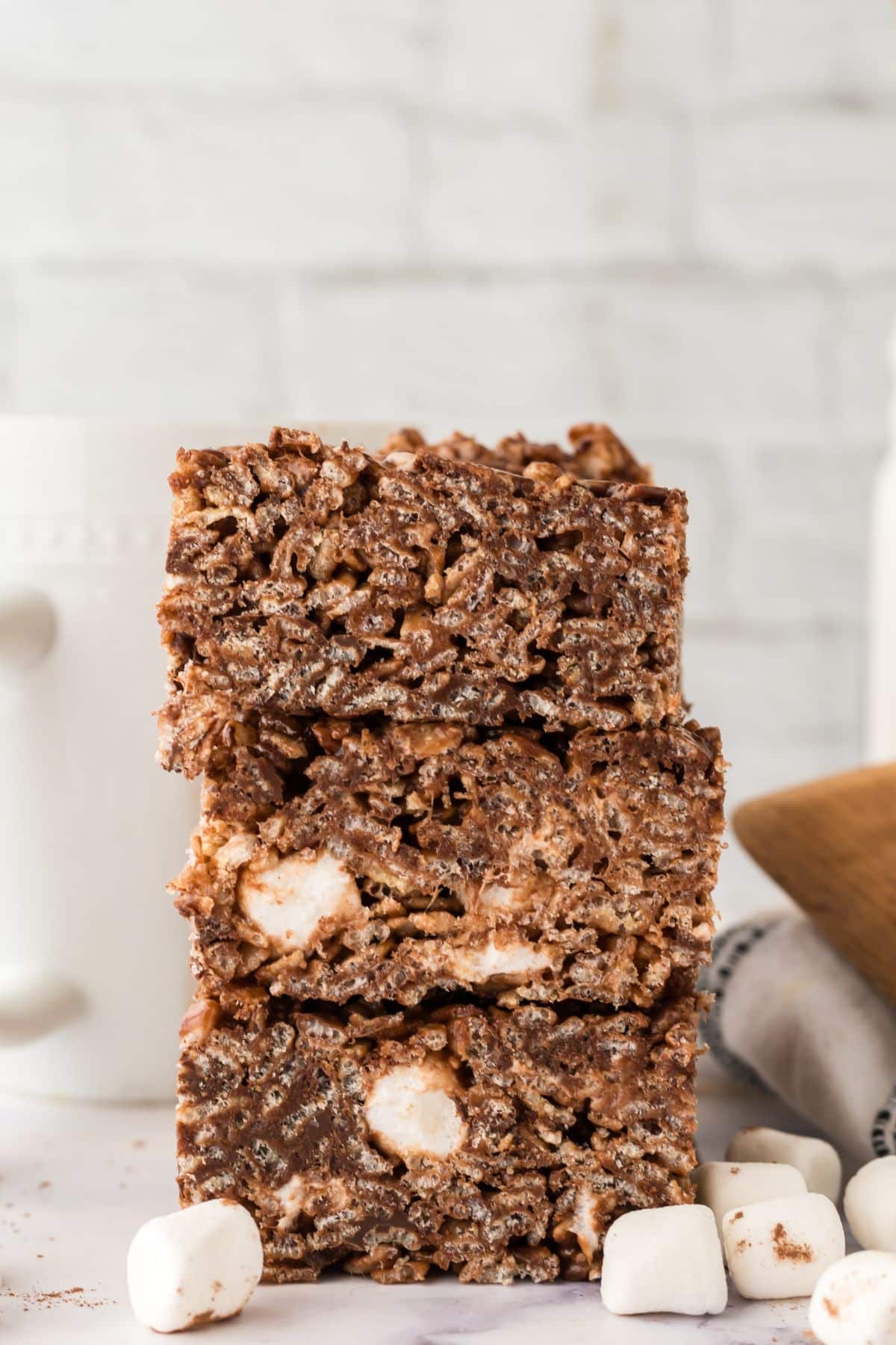 A stack of chocolate rice krispies squares with marshmallows and a cup of coffee in the background