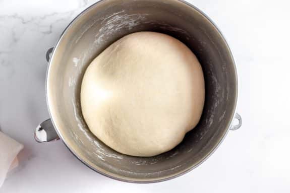 Dough in a metal bowl on a marble countertop.