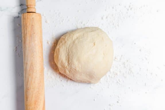 A dough ball and a wooden rolling pin on a marble table.