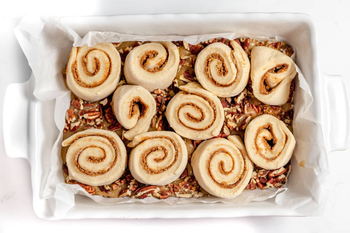 Cinnamon rolls in a white dish with pecans on top.