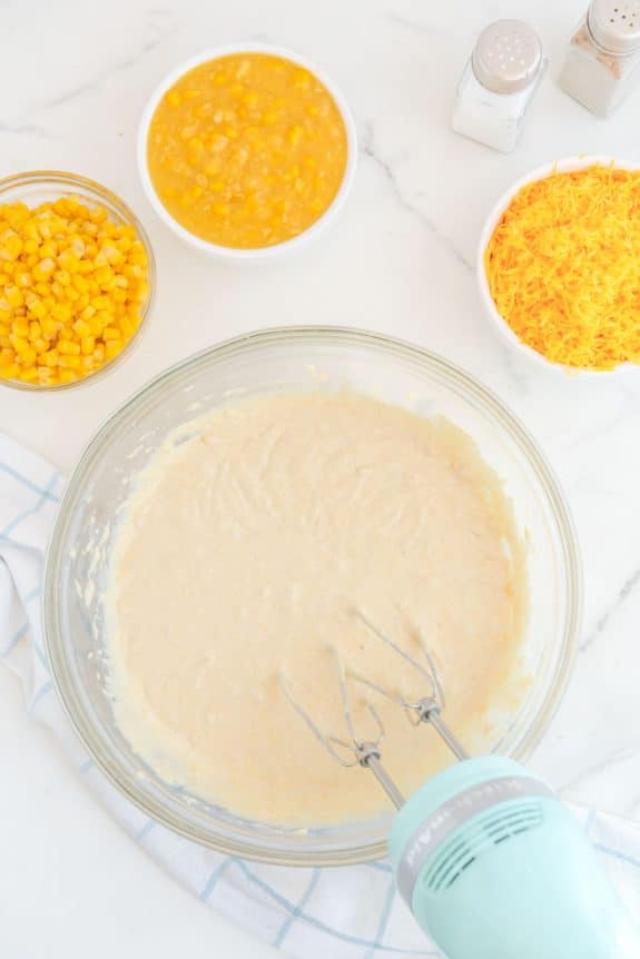 A bowl of cornmeal batter with a mixer and other ingredients.