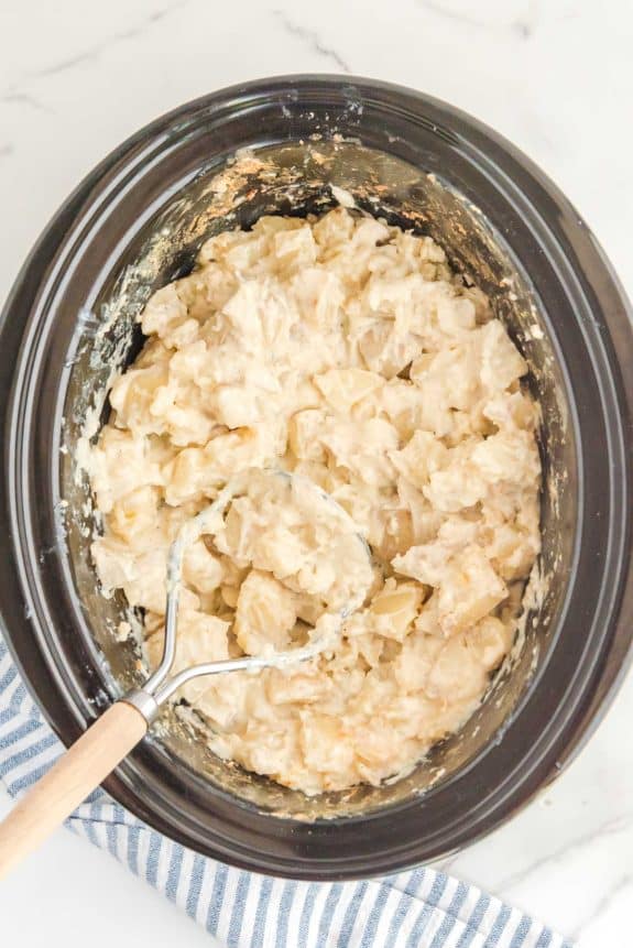 Mashed potatoes in a crock pot with a wooden spoon.