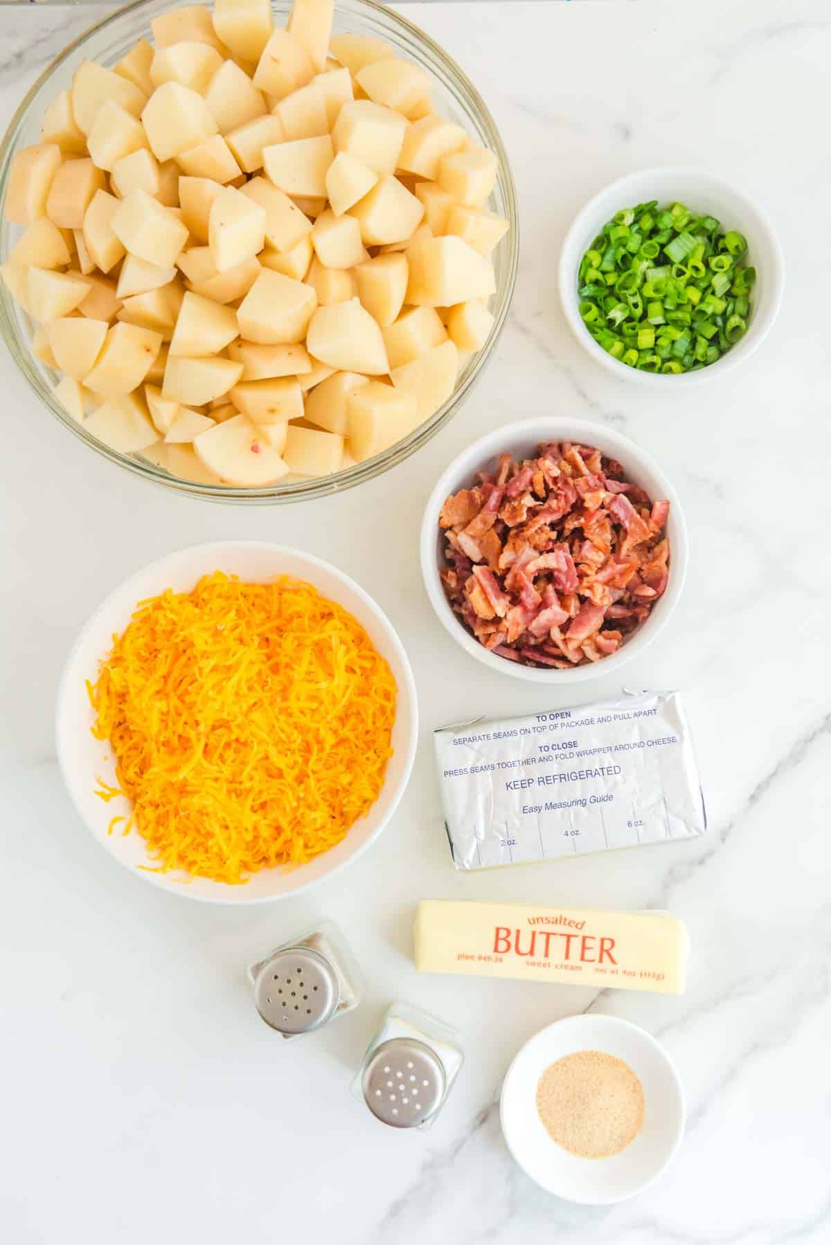 The ingredients for loaded mashed potatoes are laid out on a marble countertop.