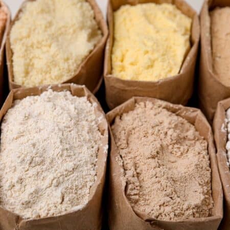 Various types of flour displayed in paper bags, including white, whole wheat, and specialty grains.