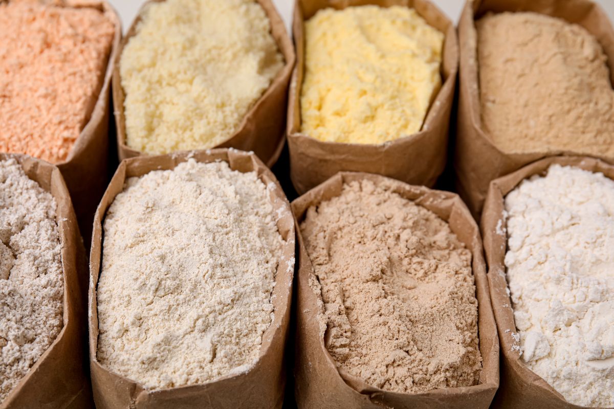 Various types of flour displayed in paper bags, including white, whole wheat, and specialty grains.