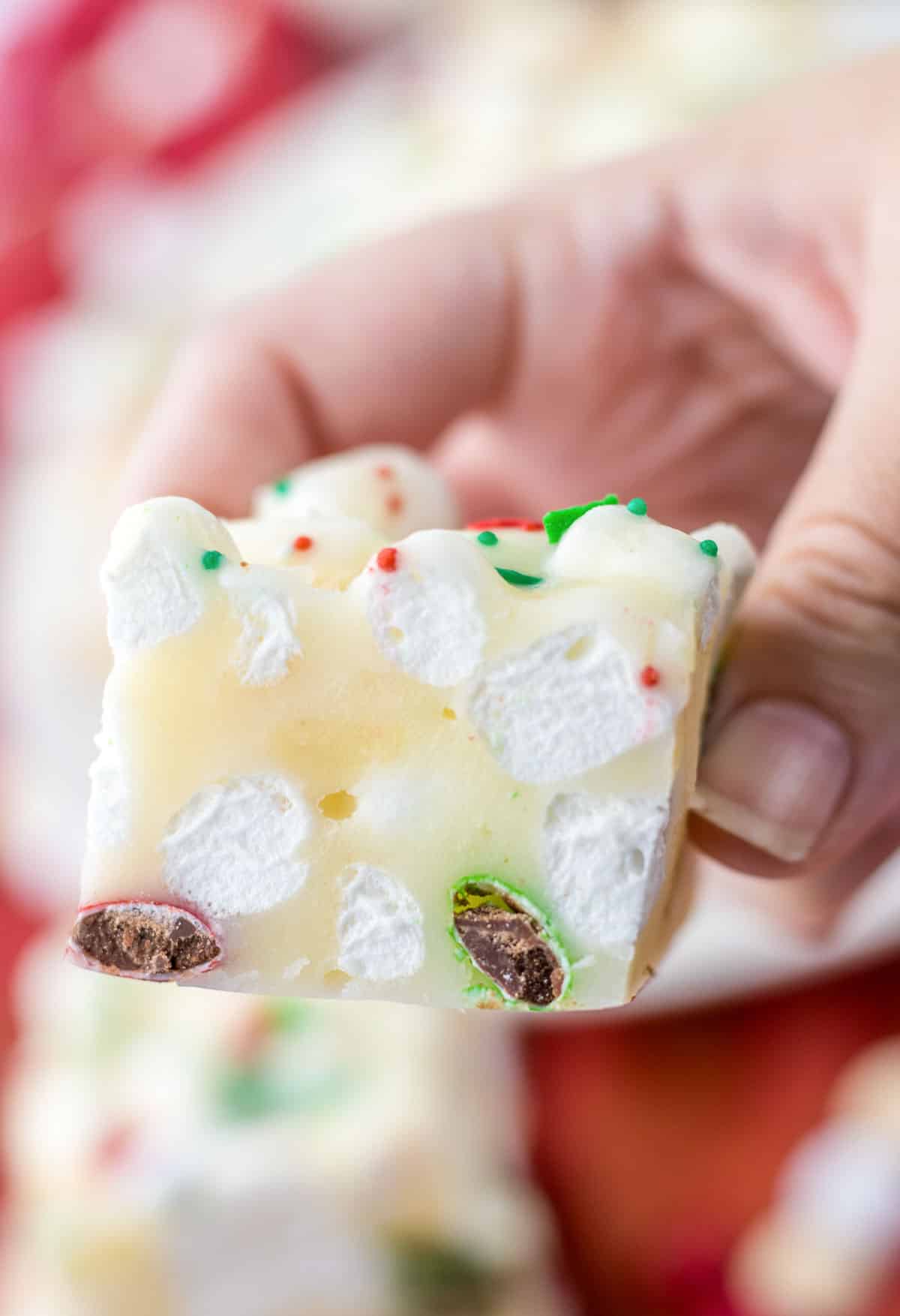 A person holding a piece of white chocolate rocky road showing marshmallows in it