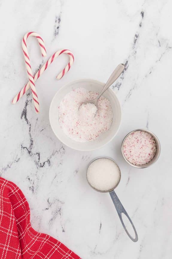A bowl of sugar and candy canes on a marble table.