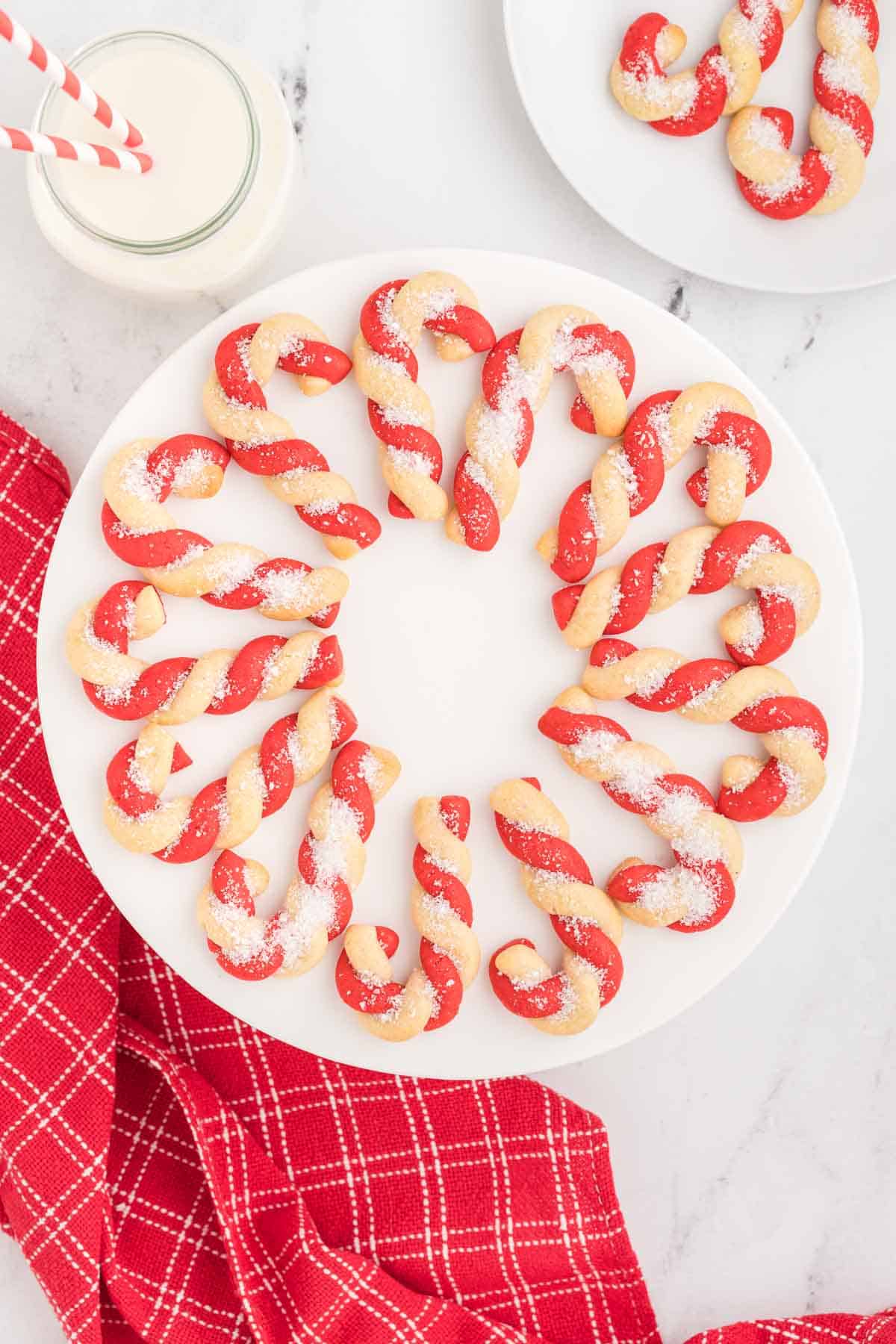 Candy cane cookies on a plate next to a glass of milk.