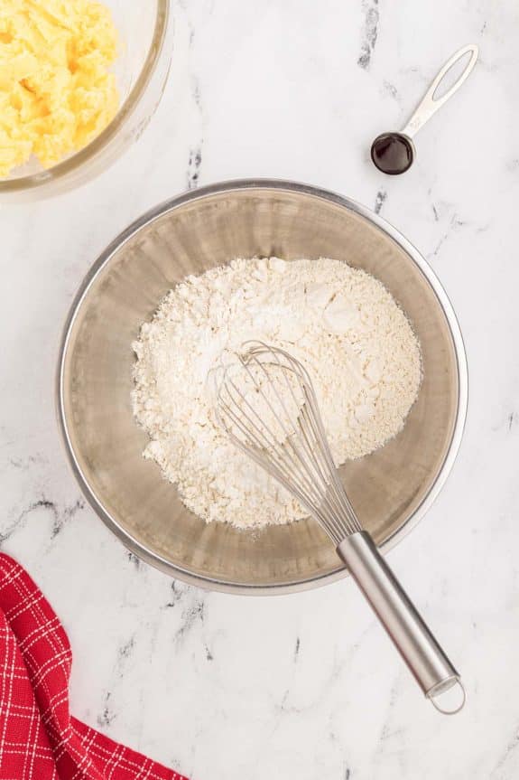 A mixing bowl with eggs, flour, and whisk.