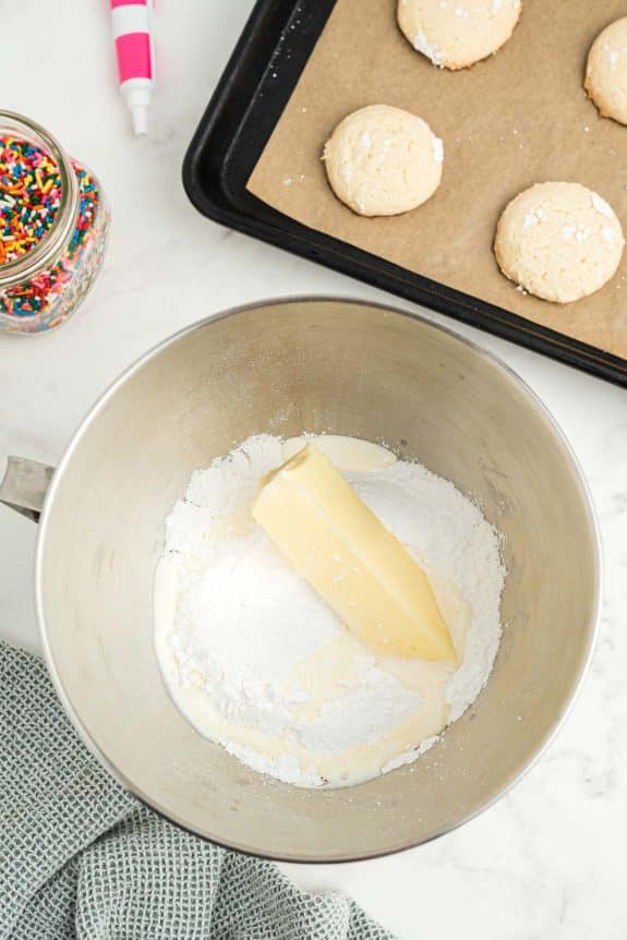 A bowl of flour, sugar, and butter next to a baking sheet.