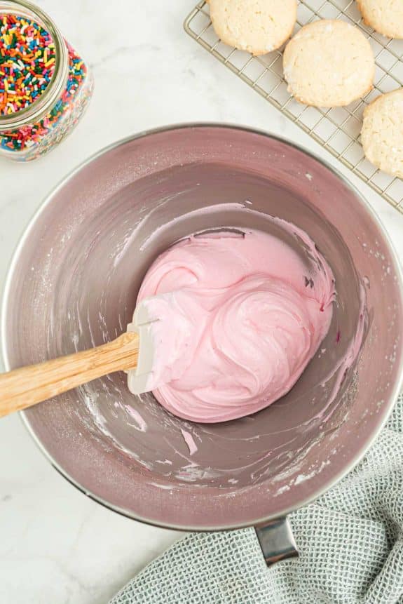 Pink icing in a mixing bowl with a wooden spoon.