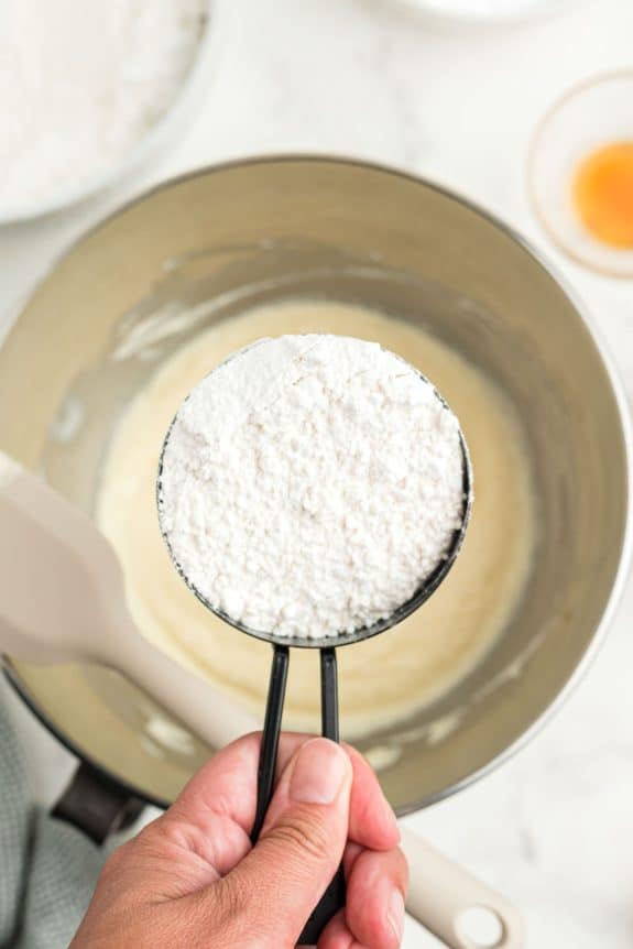 A person holding a spoonful of flour in a pan.