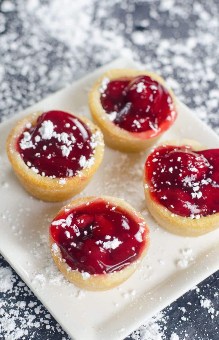 Four cherry tarts with powdered sugar on a white plate.