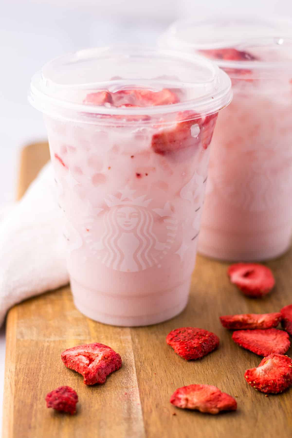 Two cups of Copycat Starbucks Pink Drink with frozen strawberries on a wooden table.