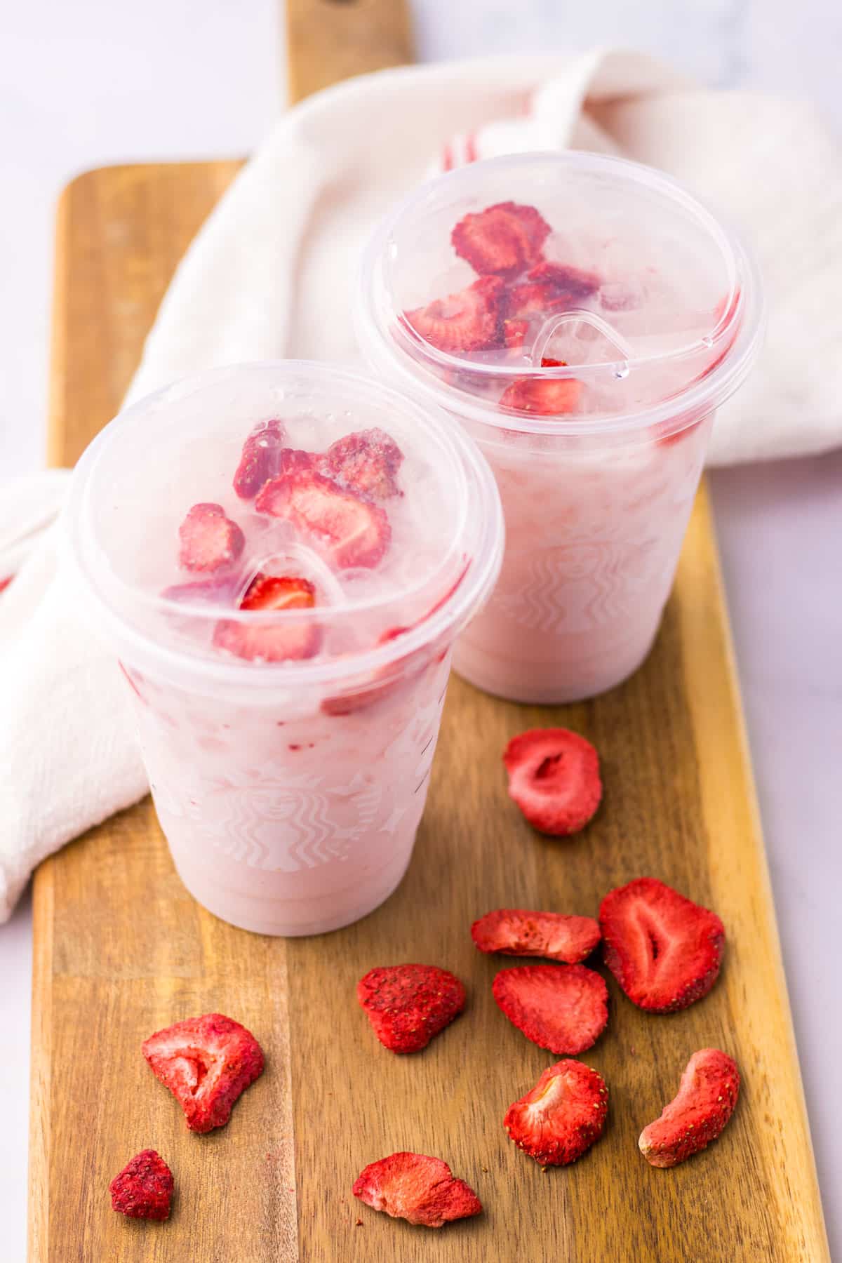 Cups of Copycat Starbucks Pink Drink with strawberries on a wooden board.