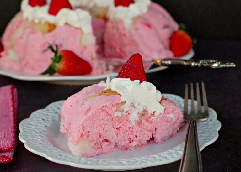 A pink bundt cake with strawberries and whipped cream on a plate.