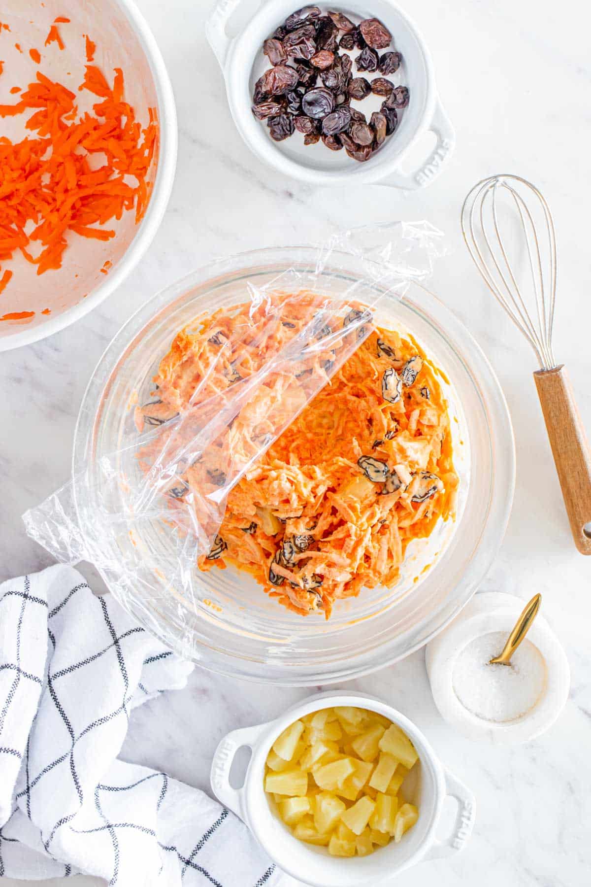 A bowl of carrot raisin salad with plastic wrap.