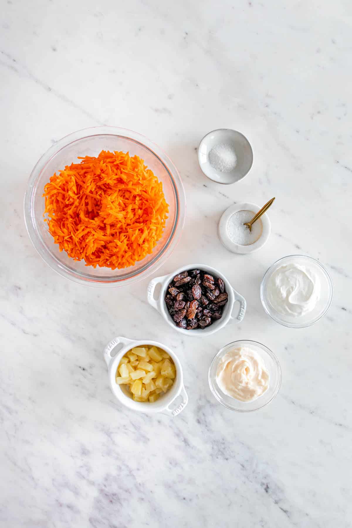 A bowl of carrots, raisins and other ingredients on a marble countertop.