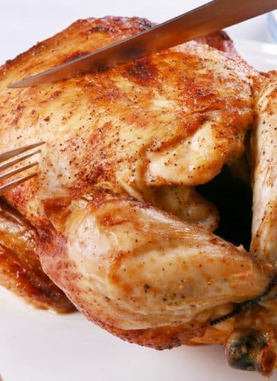 A person is cutting a roasted chicken with a fork, demonstrating how to reheat a rotisserie chicken.