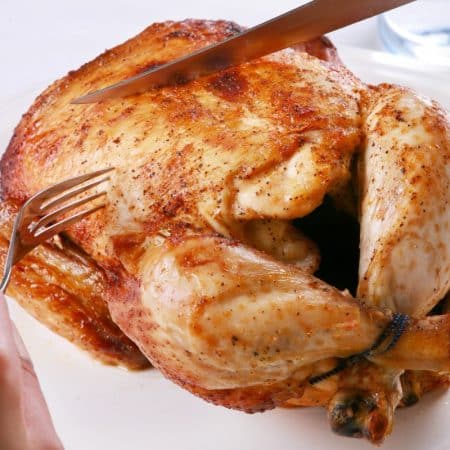 A person is cutting a roasted chicken with a fork, demonstrating how to reheat a rotisserie chicken.