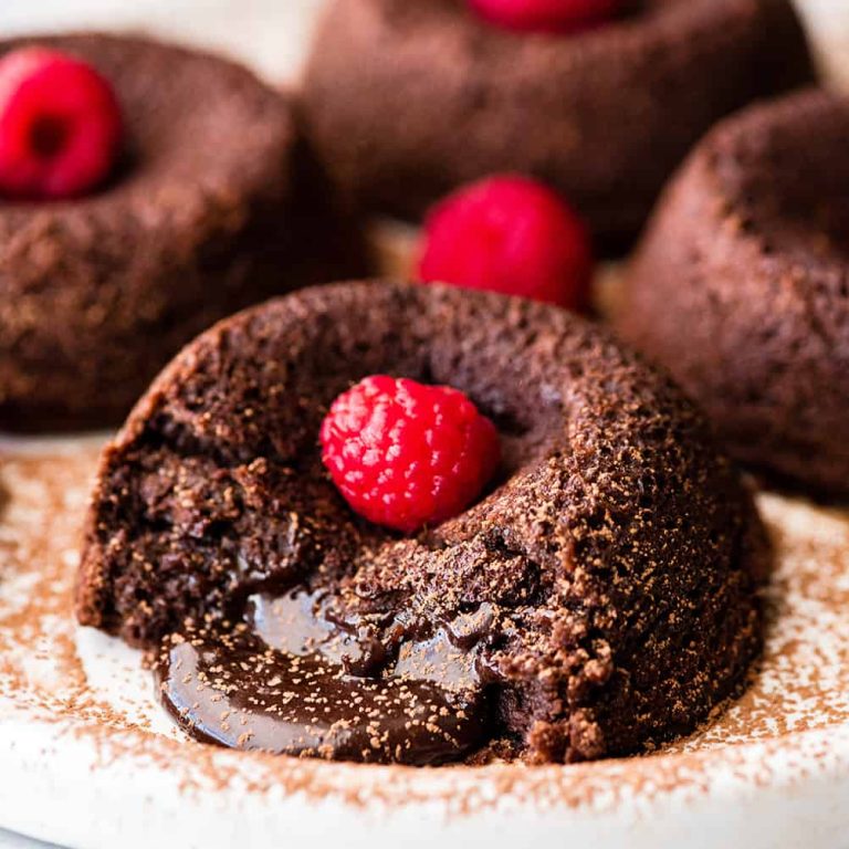 A plate of chocolate cupcakes with raspberries on top.