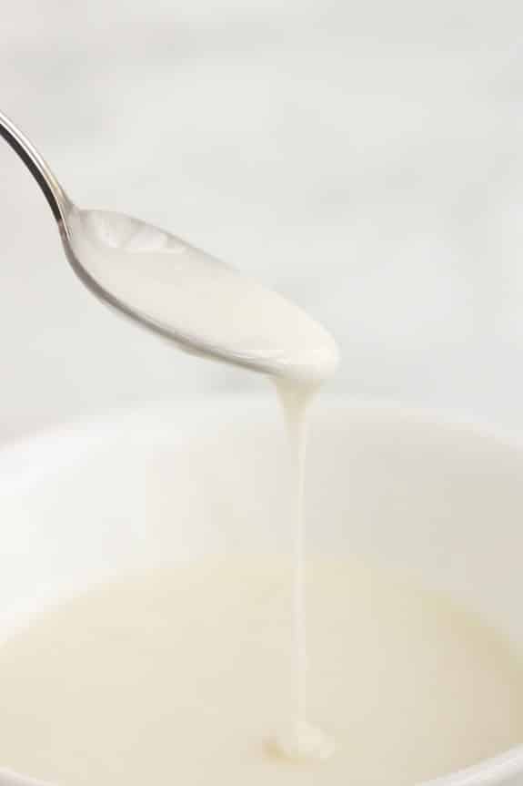 A spoon is pouring milk into a bowl.