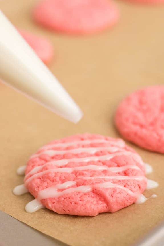 Pink icing being poured onto a cookie sheet.