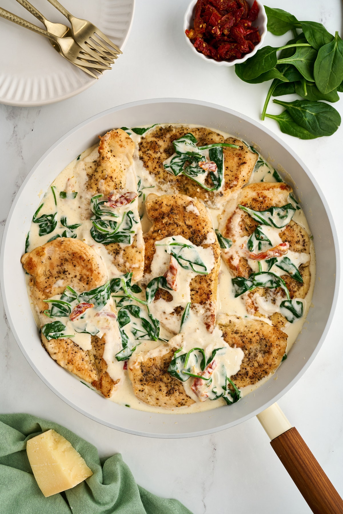A pan of chicken florentine with cheese, spinach and other ingredients on the side.