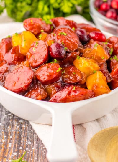 Slow cooker cranberry pineapple kielbasa in a white bowl with ingredients on the side.