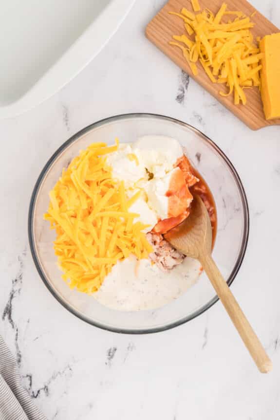 A bowl with cream cheese, cheddar cheese and a spoon next to it.