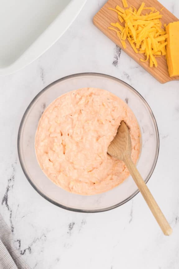 A bowl of cheesy dip with a wooden spoon.