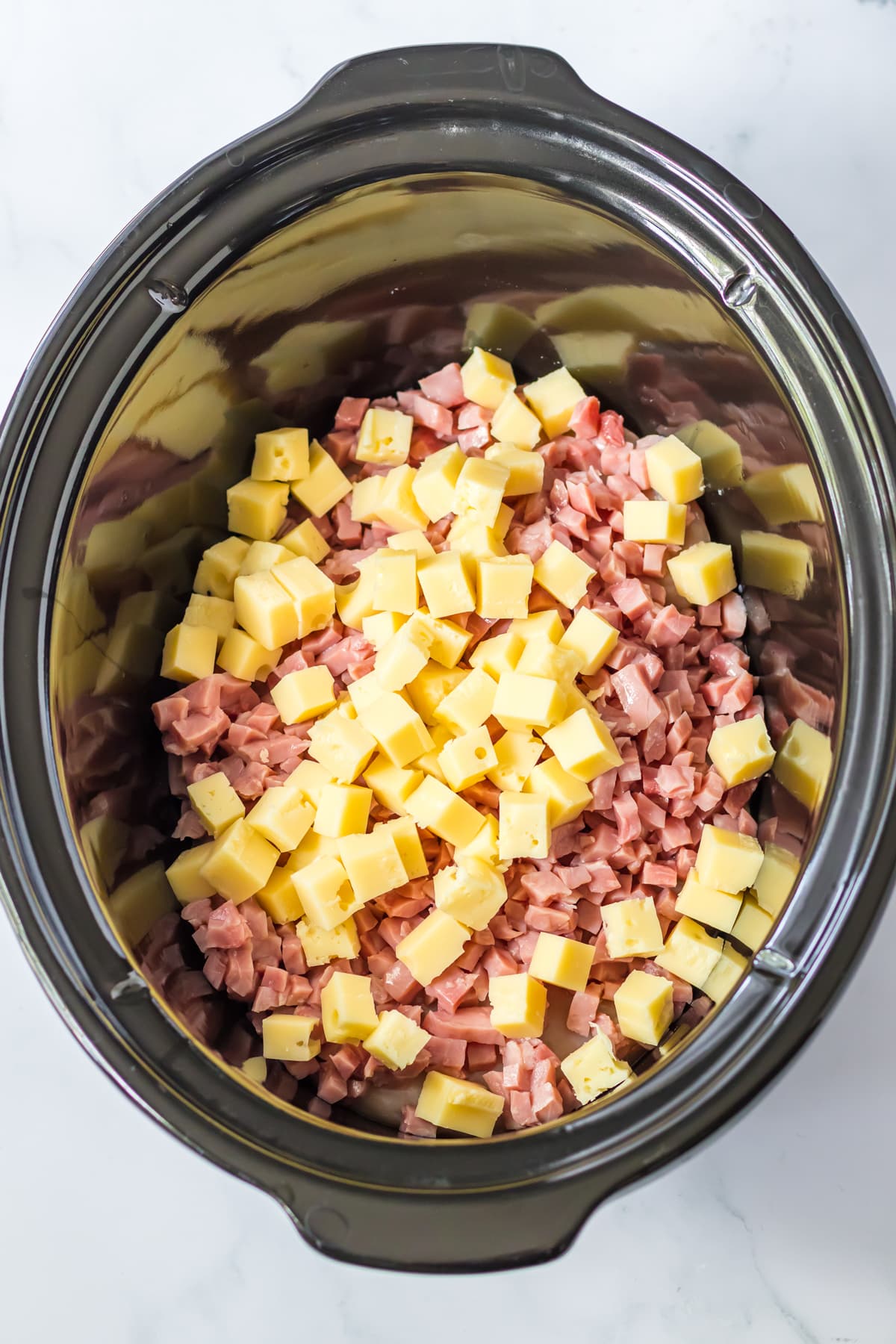 Adding ham and cheese in a slow cooker is a step in preparing Slow Cooker Chicken Cordon Bleu