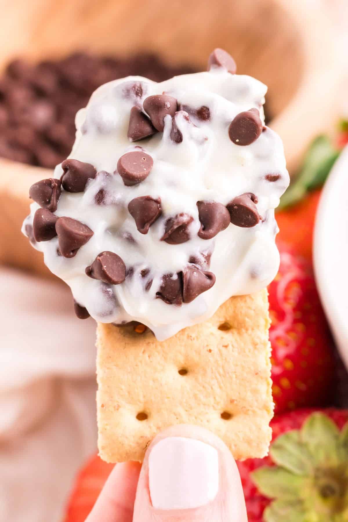 A person holding a cracker topped with cannoli dip and strawberries.