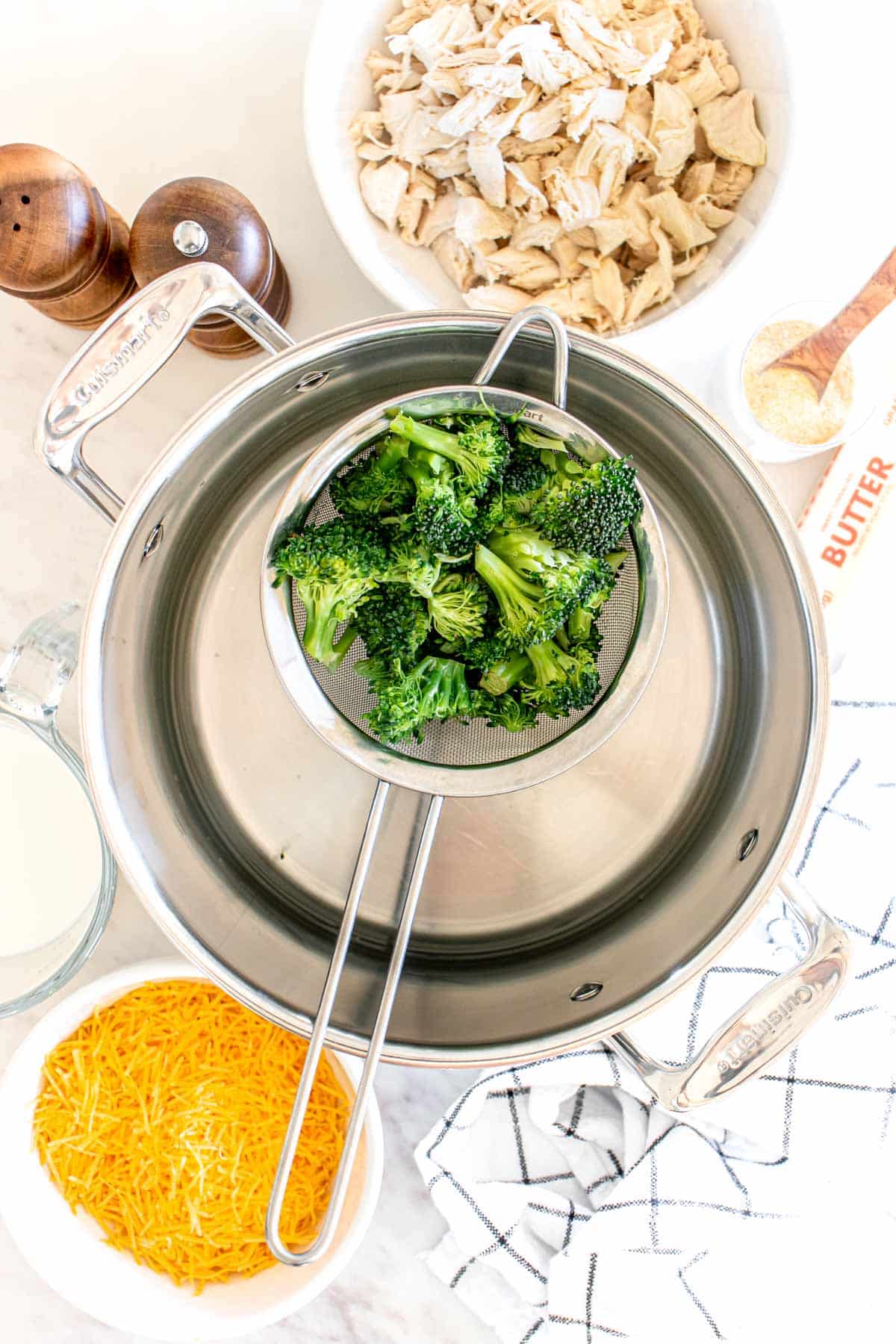 A bowl of broccoli over pan with side of shredded chicken