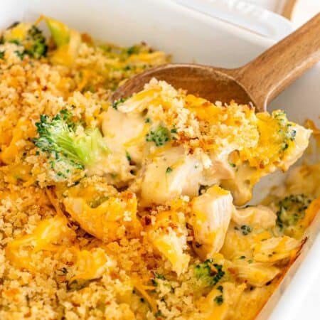 Chicken divan and broccoli casserole in a white dish with a wooden spoon.