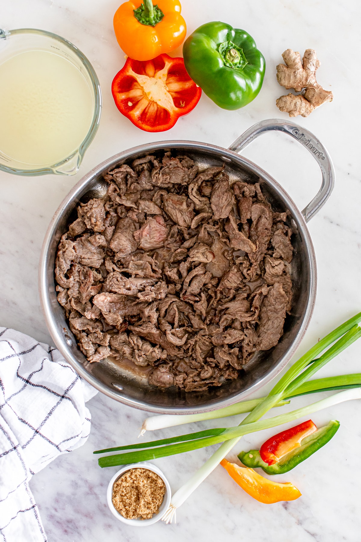 Sautéed beef in a pan surrounded by ingredients like bell peppers, ginger, green onions, and brown sugar.