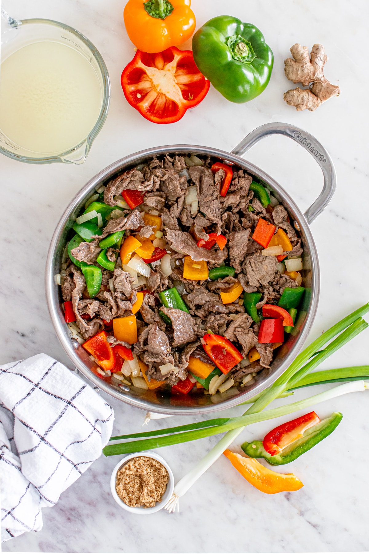 Next process in preparing Chinese Pepper Steak is to stir-fry beef with bell peppers and onions in a pan, surrounded by fresh ingredients and a glass of corn starch.