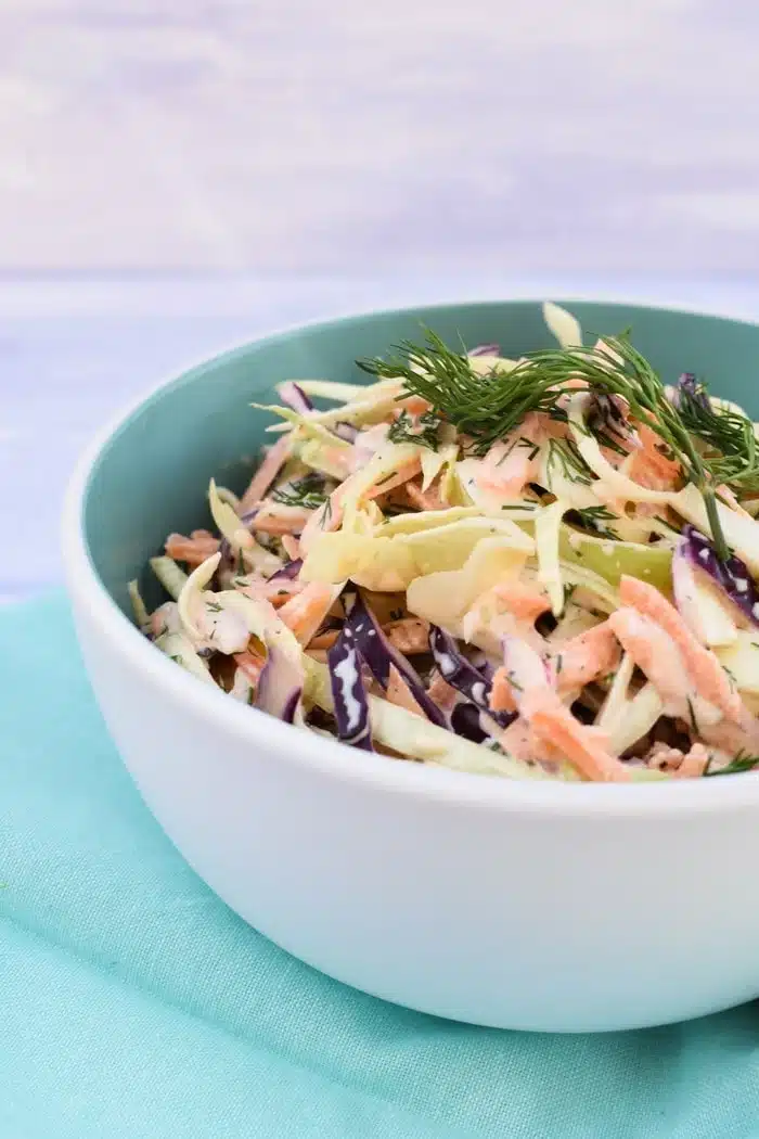 A bowl of coleslaw with dill on a blue background.