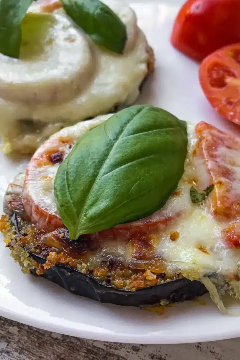 Two eggplant pizzas with tomatoes and basil on a plate.