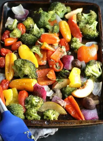 Roasted vegetables on a baking sheet with a blue spatula.