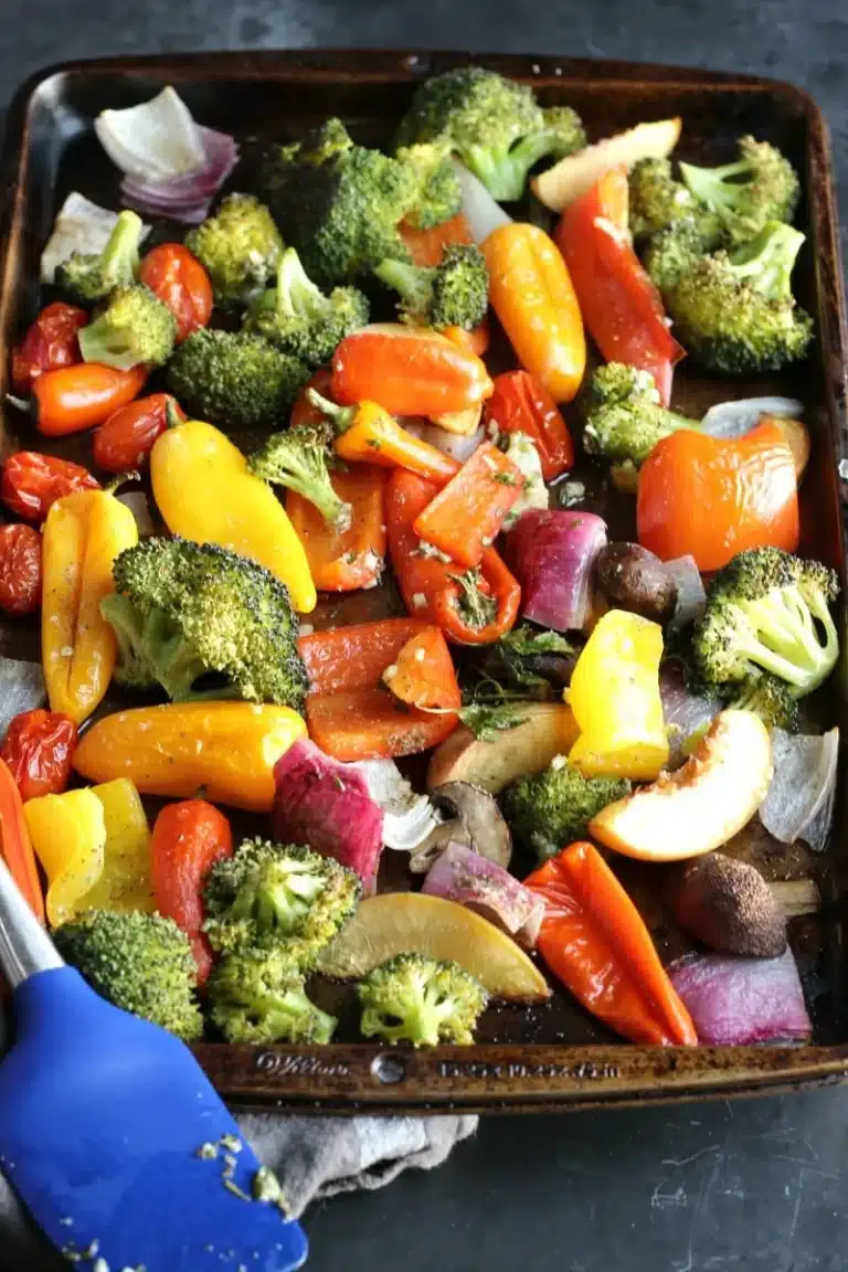 Roasted vegetables on a baking sheet with a blue spatula.