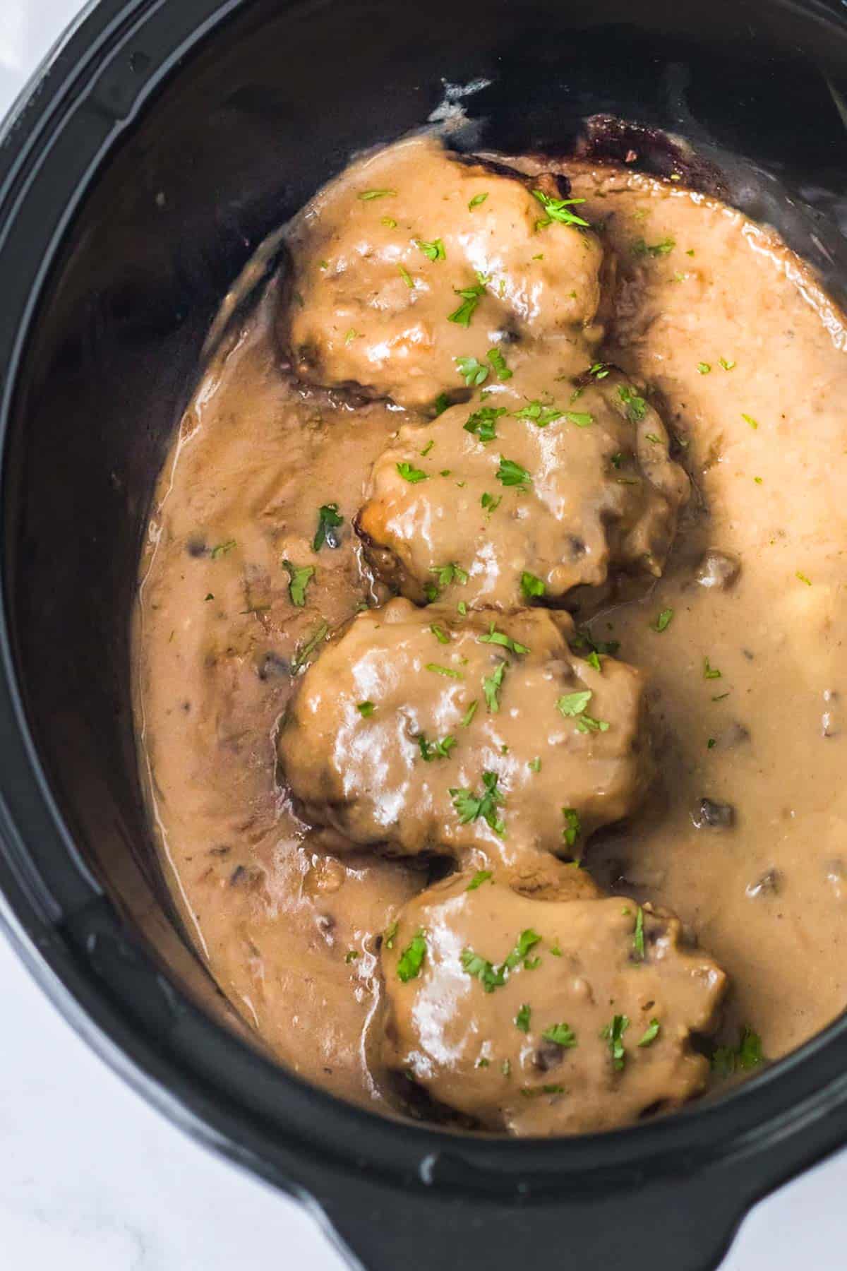 A slow cooker filled with smothered meatballs and gravy.