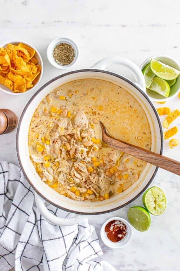 A pot of white chicken chili topped with cheese, served with lime wedges and tortilla chips on the side.