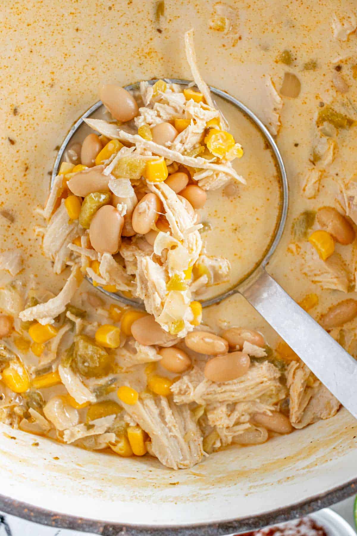 A ladle scooping white chicken chili with corn and beans from a pot.