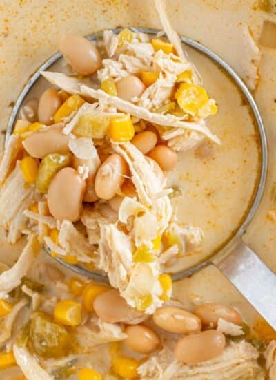 A ladle scooping up white chicken chili with beans and corn.