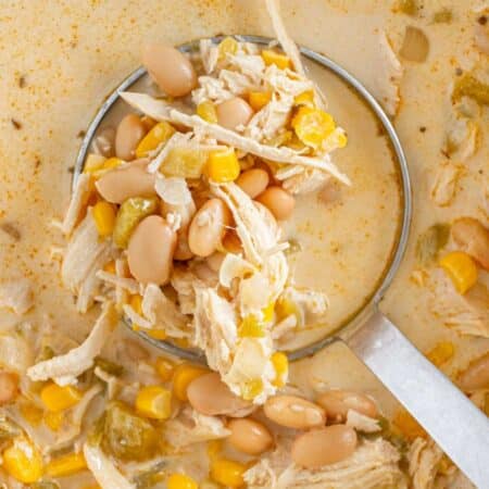 A ladle scooping up white chicken chili with beans and corn.